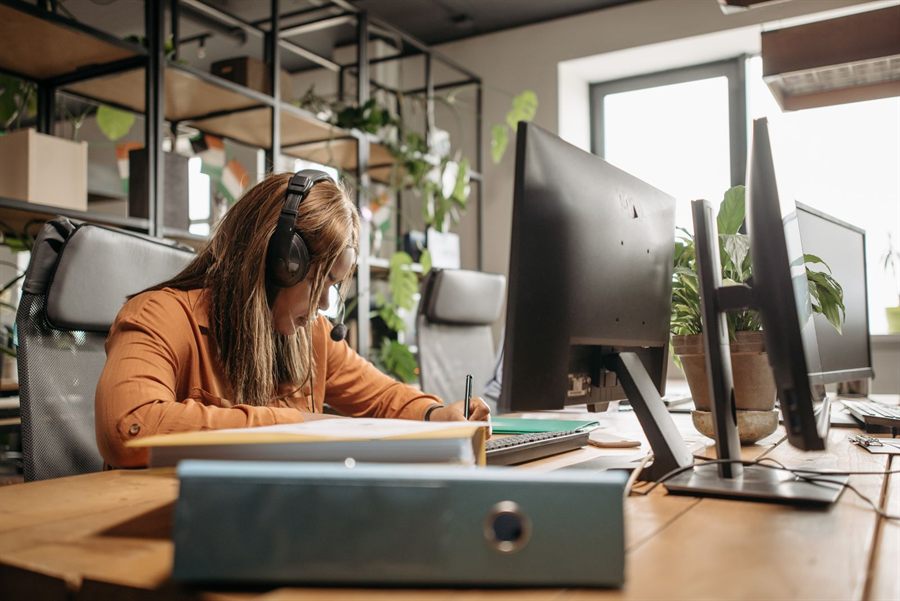 Woman with headphones working at a desk with computer screens