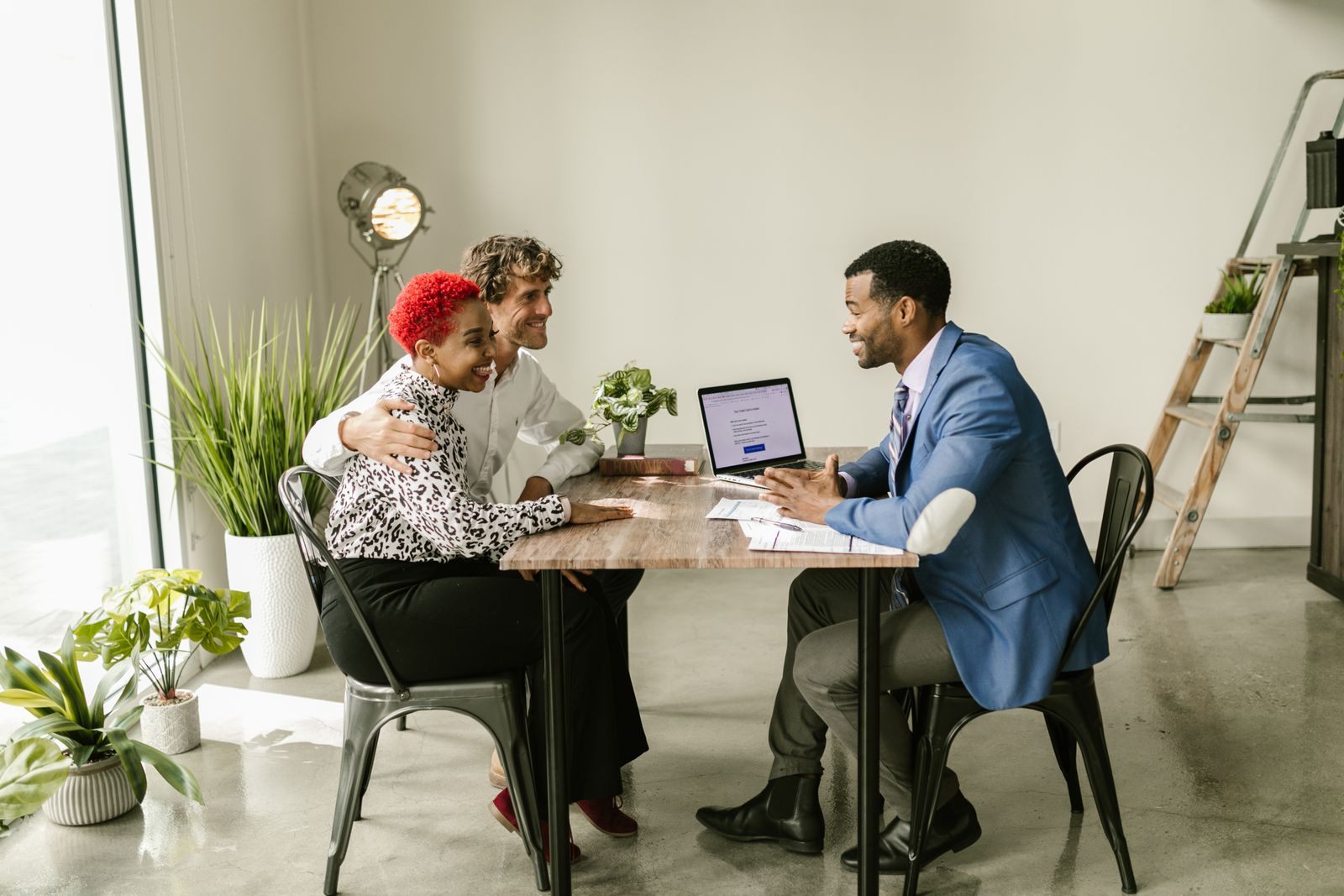 A couple meeting an advisor across a table in a bright office with potted plants