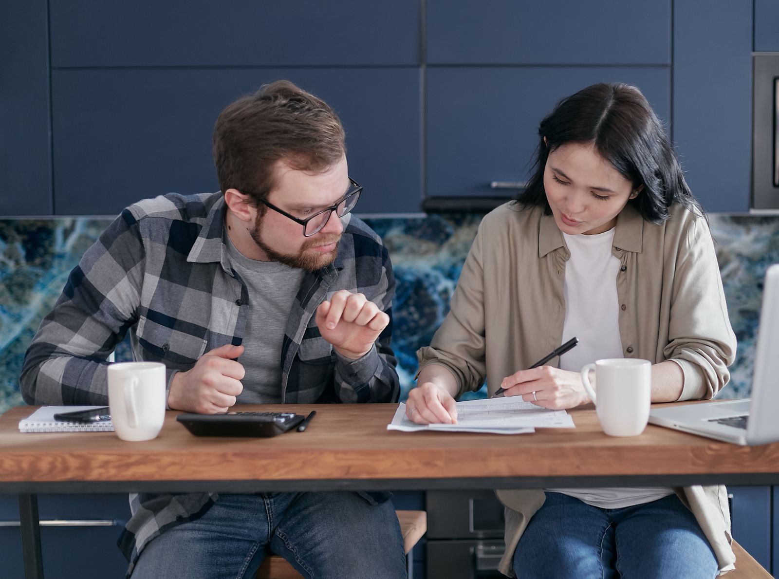 A couple at a table reading documents, with a calculator and coffee mugs