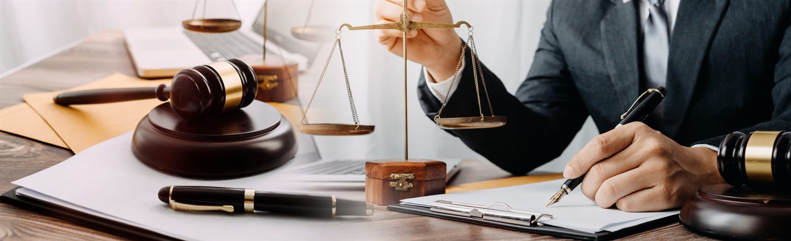 A gavel and scales of justice on a desk beside a person signing papers